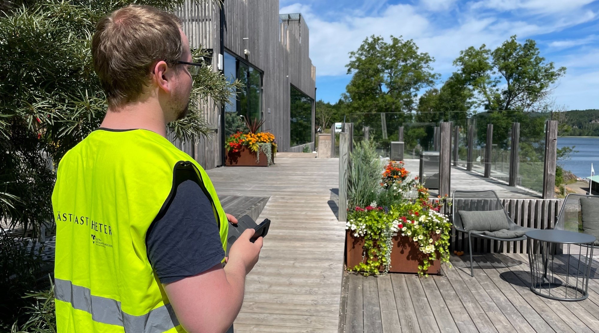 En man med gul väst inventerar i mobilen på en uteplats.